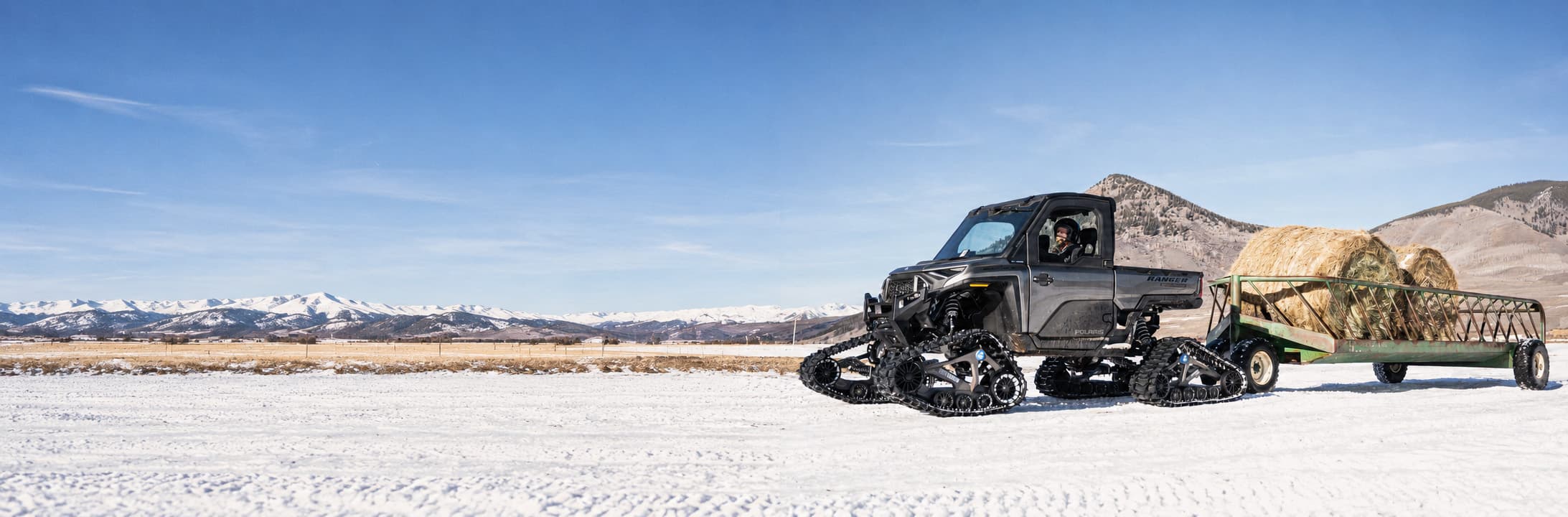 A Polaris Ranger on Camso ENDUR tracks pulling a trailer of hay bales across a snow-covered ranch